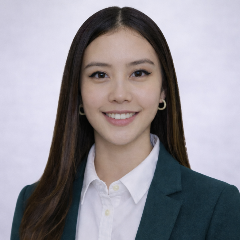 A young woman with long dark hair, wearing a white collared shirt and a dark green blazer, smiling against a plain light background.